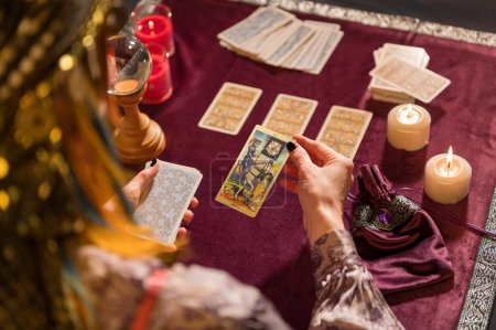 Rückansicht der Ernte unkenntlich weibliche Wahrsagerin im Kostüm Kommissionierung Tod Tarotkarte, während sie am Tisch mit brennenden Kerzen und Kristall sitzen