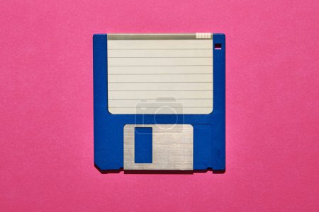 Téléchargez les photos : Vue du dessus du papier vierge avec des lignes collées sur disquette bleue sur fond rose - en image libre de droit