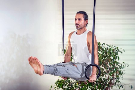 Foto de Hombre adulto haciendo ejercicio L Sit con anillos contra macetas en casa durante el entrenamiento de fitness - Imagen libre de derechos