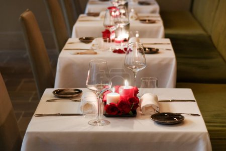 Foto de Fila de mesas decoradas con velas encendidas y anteojos vacíos sobre mantel blanco en restaurante de lujo - Imagen libre de derechos