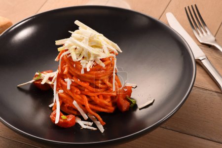Foto de Apetitiva pasta de espaguetis con salsa de tomate y parmesano servido en plato negro sobre mesa de madera en el restaurante - Imagen libre de derechos