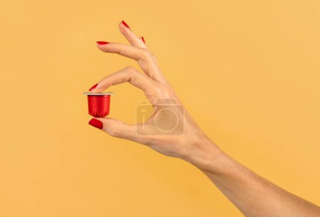 Foto de Primer plano de la mano de la mujer anónima de la cosecha sosteniendo cápsula de café rojo sobre fondo amarillo en el estudio - Imagen libre de derechos