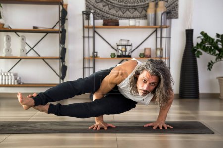 Focused adult male doing Eight Angle asana on mat while practicing fitness exercise at home