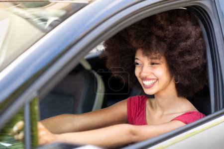 Foto de Sonriendo emocionada joven étnica femenina con pelo negro Afro coche de conducción en el día de verano en la ciudad - Imagen libre de derechos