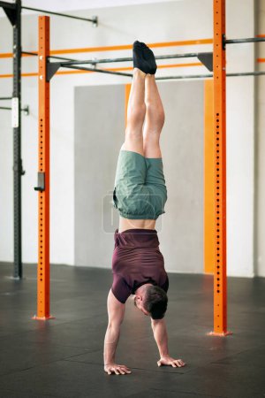 Foto de Anónimo hombre fuerte estiramiento del cuerpo en posición invertida durante el entrenamiento cerca de la barra de fitness en el moderno gimnasio estudio - Imagen libre de derechos