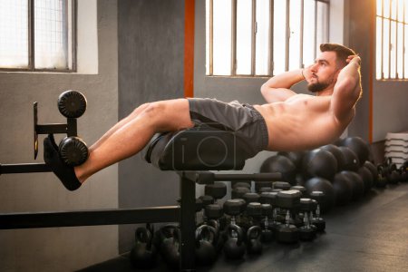Foto de Vista lateral de los músculos masculinos haciendo GHD sentarse ejercicio para abdominales en el gimnasio moderno con equipo de fitness - Imagen libre de derechos