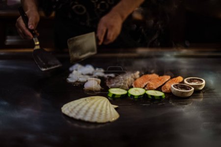 Téléchargez les photos : Spectacle teppan dans un restaurant japonais traditionnel. les mains du cuisinier. cuisinier japonais prépare de la viande, du poisson, du riz, des légumes pour les invités - en image libre de droit