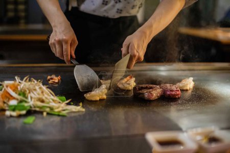 Téléchargez les photos : Spectacle teppan dans un restaurant japonais traditionnel. les mains du cuisinier. cuisinier japonais prépare de la viande, du poisson, du riz, des légumes pour les invités - en image libre de droit