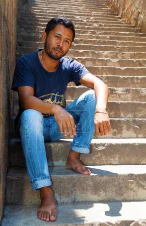Foto de Primer plano retrato joven guapo malgache chico sonriendo, sentado en las escaleras, hablando de teléfono. - Imagen libre de derechos