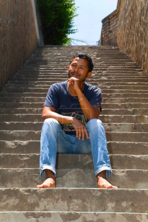 Foto de Primer plano retrato joven guapo malgache chico sonriendo, sentado en las escaleras, hablando de teléfono. - Imagen libre de derechos