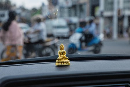 Photo for Buddha figurine on the hood of a car. tuk tuk driver in sri lanka. Small golden Buddha figurine against the background of the window - Royalty Free Image