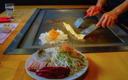 Téléchargez les photos : Mains du chef avec spatule sur teppanyaki. cuisson des légumes viande et fruits de mer sur la table chaude hibachi grill. Cuisine japonaise traditionnelle. Spectacle Teppan - en image libre de droit
