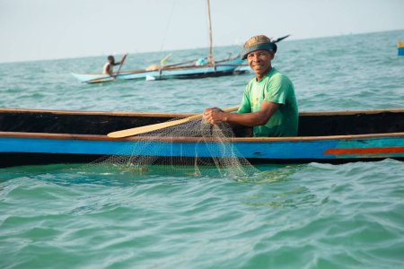 Foto de Morondava,Madagascar . 18 octubre 2023. Pescador malgache en barco piragua viejo de madera casera en el océano captura peces con red. enfoque selectivo, vista de cerca desde el océano - Imagen libre de derechos