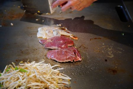 chef's hands with spatula over teppanyaki. cooking vegetables meat and seafood on hot hibachi grill table. Traditional Japanese. Teppan show. cuisine peoples of world concept