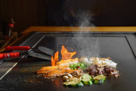 chef's hands with spatula over teppanyaki. cooking vegetables meat and seafood on hot hibachi grill table. Traditional Japanese Cuisine. Teppan show
