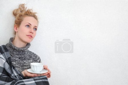 Photo for A young woman enjoying a moment of relaxation, seated on the floor and leaning against a white wall with a cup of coffee or tea. Calm and cozy atmosphere for lifestyle or beverage-related concepts. - Royalty Free Image