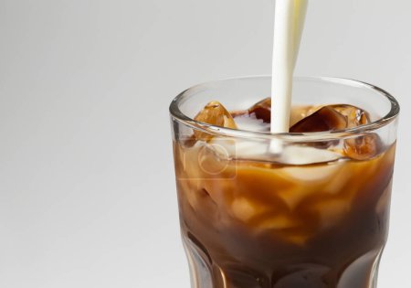 Milk poured over Iced Coffee on white backgroun