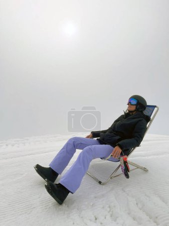 Photo for Woman sitting on the top of the mountain in a chair, fog around, a break from snowboarding. Alps, mountain sports, snowboarding. - Royalty Free Image