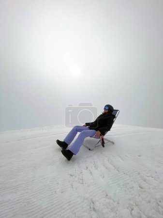 Photo for Woman sitting on the top of the mountain in a chair, fog around, a break from snowboarding. Alps, mountain sports, snowboarding. - Royalty Free Image