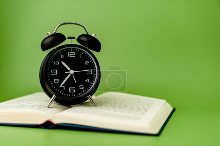 Foto de Despertador negro Ponga en un libro abierto, ideas de lectura y tiempo de lectura. - Imagen libre de derechos