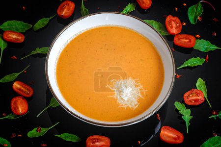 Téléchargez les photos : Soupe à la crème de potiron et carotte au fromage dans un bol blanc. Fond sombre avec roquette et tomates. Gros plan. Vue du dessus. - en image libre de droit