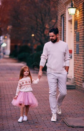Téléchargez les photos : Happy father and daughter walking on the evening street in a town - en image libre de droit