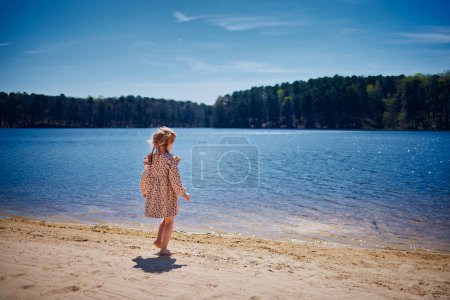 Foto de Niña despreocupada caminando a lo largo del lago en el soleado día de primavera - Imagen libre de derechos
