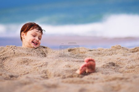 Téléchargez les photos : Mignon riant enfant couché dans le sable, profiter de l'été sur la plage - en image libre de droit
