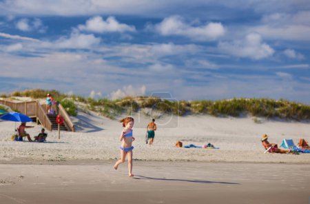 Photo for People relaxing at sandy beach on sunny summer day. cute little girl running to the water. summer vacation - Royalty Free Image