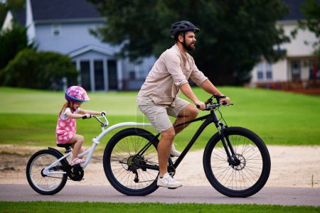 Téléchargez les photos : Père et fille, jeune enfant faisant du vélo ensemble. balade à vélo avec remorque à vélo remorquable. mode de vie actif pour les familles avec enfants - en image libre de droit