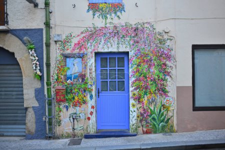 Téléchargez les photos : Une entrée ornée à une maison dans une vieille rue française peinte avec des peintures trompe l'oeil de fleurs, de fausses fenêtres, des chaises et un perroquet - en image libre de droit