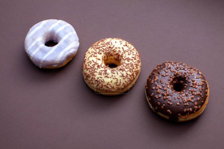 Téléchargez les photos : Trois beignets anneaux isolés sur fond brun - en image libre de droit