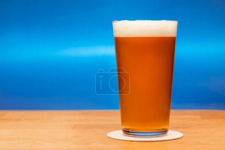 Foto de Full shaker pint glass of amber ale or beer on wooden table with grey background - Imagen libre de derechos