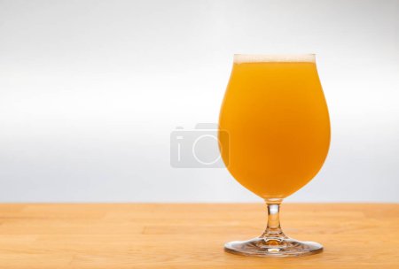 Foto de Full snifter glass of hazy New England IPA (NEIPA) pale ale beer on wooden table with grey background - Imagen libre de derechos