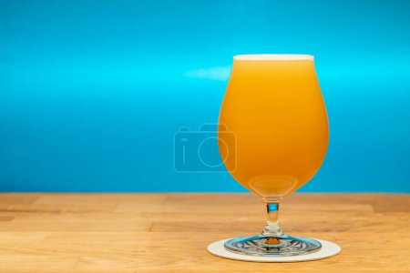Foto de Full snifter glass of hazy New England IPA (NEIPA) pale ale beer on wooden table with blue background - Imagen libre de derechos