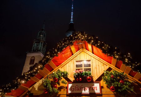 Photo for Berlin, Germany - December 13, 2018:  Illuminated Gluhwein (hot mulled wine) stall at Christmas market (Christkindlmarkt) with the Fernsehturm Television Tower seen in background - Royalty Free Image