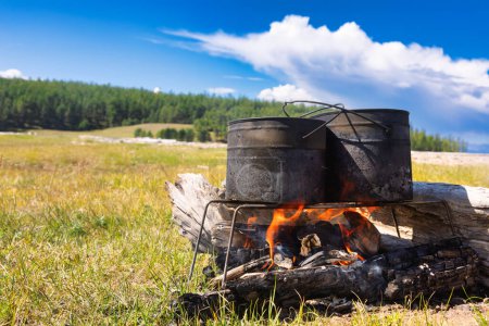 Photo for Cooking meal in pots on burning campfire during wild camping - Royalty Free Image