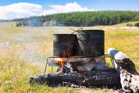 Photo for Cooking meal in pots on burning campfire during wild camping - Royalty Free Image