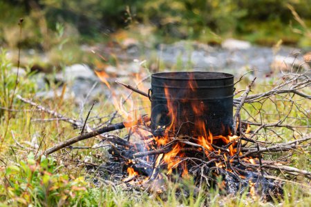 Photo for Cooking meal in pot on a burning campfire during wild camping - Royalty Free Image