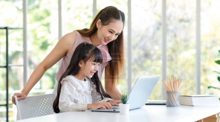 Photo for Millennial Asian happy family mother smiling helping supporting teaching little girl kid daughter studying learning doing online school homework via laptop notebook computer in living room at home. - Royalty Free Image