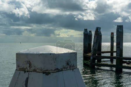 Foto de Vista de los postes de amarre del puerto de Vlieland y en el fondo el sol rompiendo a través de las nubes pesadas y reflejándose en el agua del mar de Wadden 2 - Imagen libre de derechos