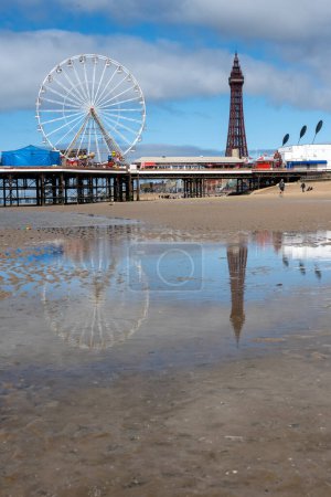 Photo for BLACKPOOL MAY 1 2023: Blackpool Tower and Central Pier are refleted in a pool left on the beach by the receding tide - Royalty Free Image