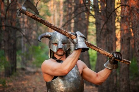 Porträt eines Kriegers mit gehörntem Helm, einem stählernen Brustpanzer mit einer beidhändigen Axt in den Händen, der vor dem Hintergrund des Waldes posiert. 