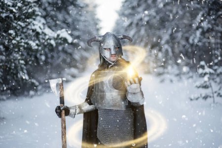 Porträt eines mittelalterlichen Fantasiekriegers mit gehörntem Helm, Brustpanzer aus Stahl, Kettenpanzer mit einer beidhändigen Axt in der Hand, der vor der Kulisse eines Winterwaldes einen Zauberspruch anwendet.