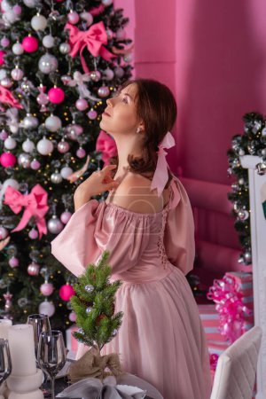 Porträt einer jungen Frau in einem rosafarbenen Kleid vor dem Hintergrund eines Weihnachtsbaums und Dekorationen.