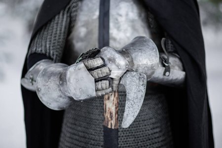 Close-up of the hands of a medieval warrior in plate gloves against the backdrop of a winter forest, selective focus.