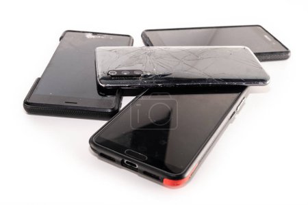 Foto de Montón de teléfonos inteligentes rotos aislados sobre fondo blanco. Teléfonos móviles dañados con pantalla agrietada. - Imagen libre de derechos