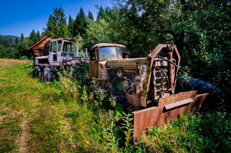 Old, wrecked machinery, abandoned snow blower and machine in the bushes. Rusty, unused, heavy vehicles in a mountain forest. Bieszczady, sunny, summer day.