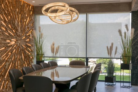 Roller blinds in the interior. Automatic solar shades large size on the window. Modern interior with wood decor panel on the wall. Green plants in hi-tech flower pots. Electric sunscreen curtains for