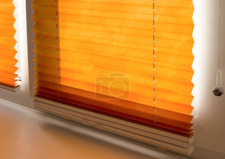 Téléchargez les photos : Stores plissés avec tissu plié orange sur la fenêtre fermer. Abat-jour plissé haut vers le bas sans fil avec barre inférieure blanche. - en image libre de droit